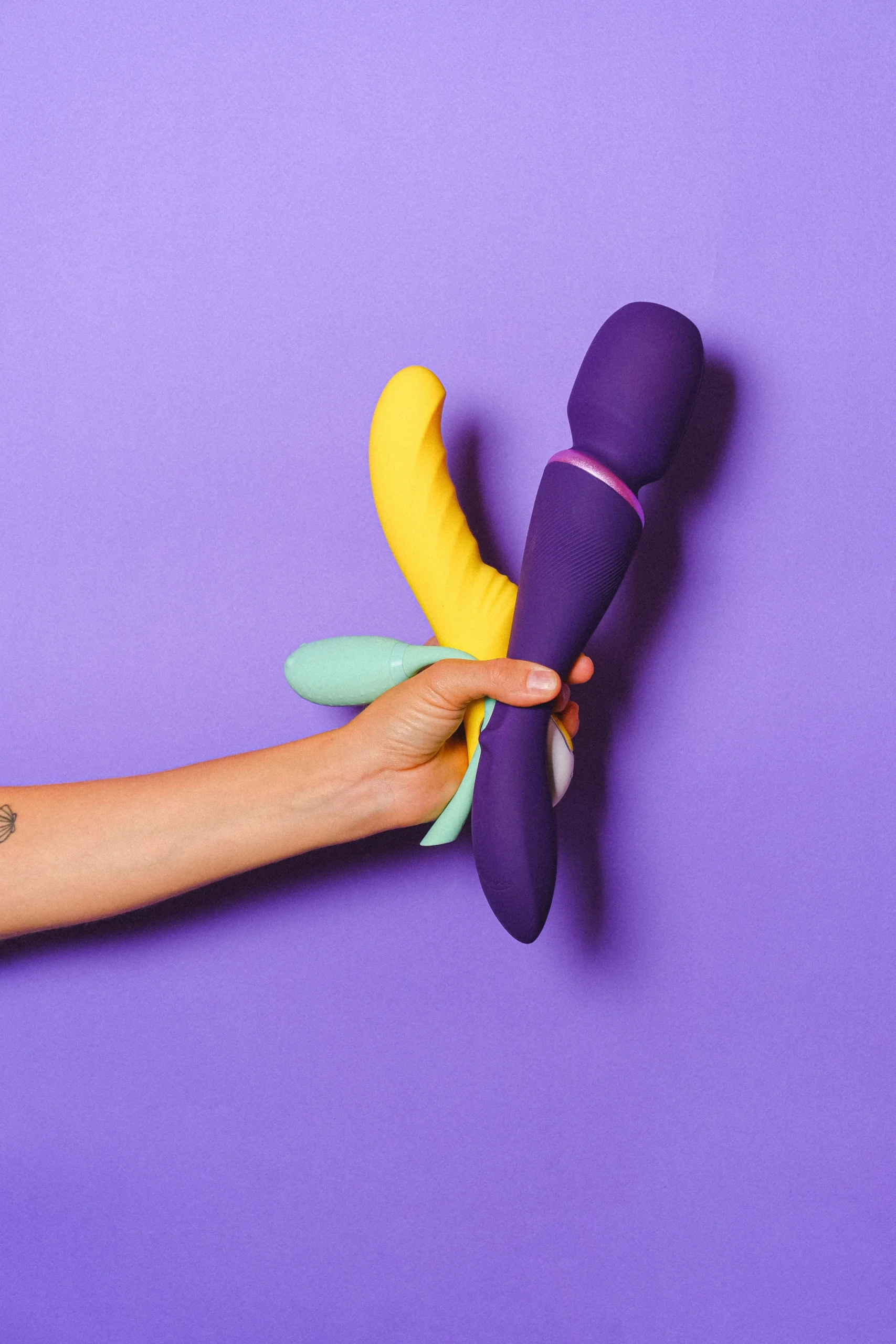 Colorful wand-style personal massagers held against a purple background